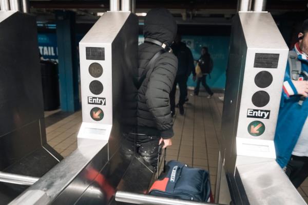 A man in a puffer jacket who jumped the turnstile and pushed a duffel bag through it