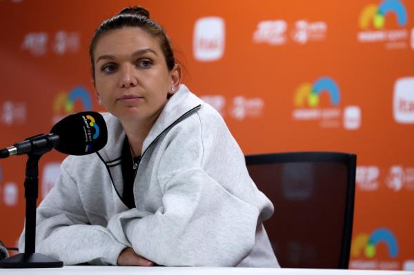 Simona Halep sitting at a table with a microphone, speaking to the media after losing a tennis match at the Miami Open.