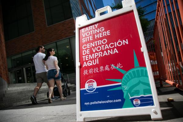 Pedestrians pass a polling station signage as early voting begins in New York, on June 15, 2024.