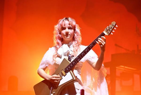 The Last Dinner Party on stage, with one member playing guitar surrounded by orange and yellow stage lighting