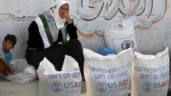 A Palestinian woman sits next to sacks of flour outside the UN Relief and Works Agency, (UNRWA) aid distribution station in Gaza City, June 20, 2007. (AP Photo/Khalil Hamra, file)